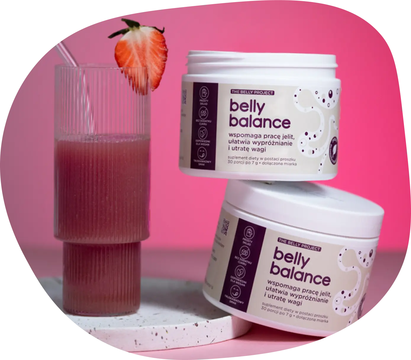 Suplement diety bellybalance wspierający prawidłową pracę jelit, obok szklanka z przygotowanym napojem koloru czerwonego oraz truskawka na brzegu szklanki.