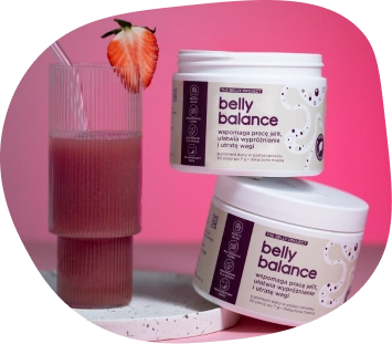 Dwa opakowania suplementu diety bellybalance obok różowego koktajlu w prążkowanej szklance ozdobionej truskawką, na różowym tle.