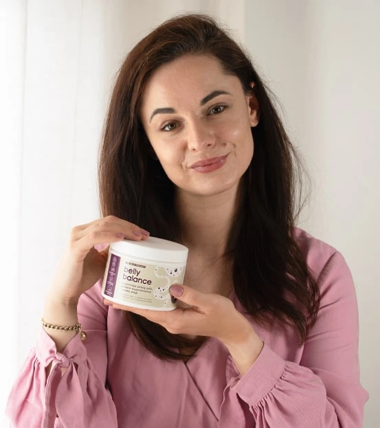 Uśmiechnięta kobieta w różowej bluzce trzymająca opakowanie suplementu diety BellyBalance
